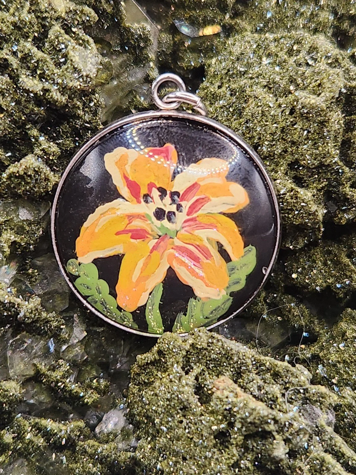 Daylily flower art pendant displayed among sparkling green crystals. Crystal display and props not included.