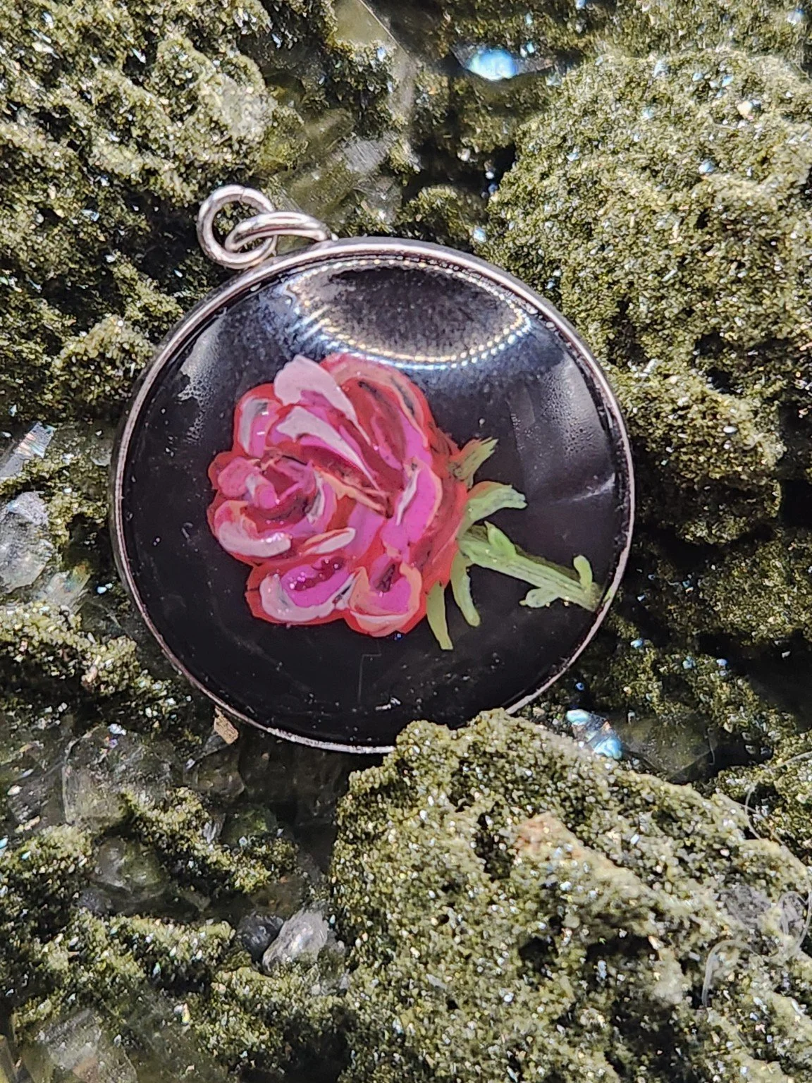 Pink rose art pendant resting on a green crystal display. Crystal display not included.