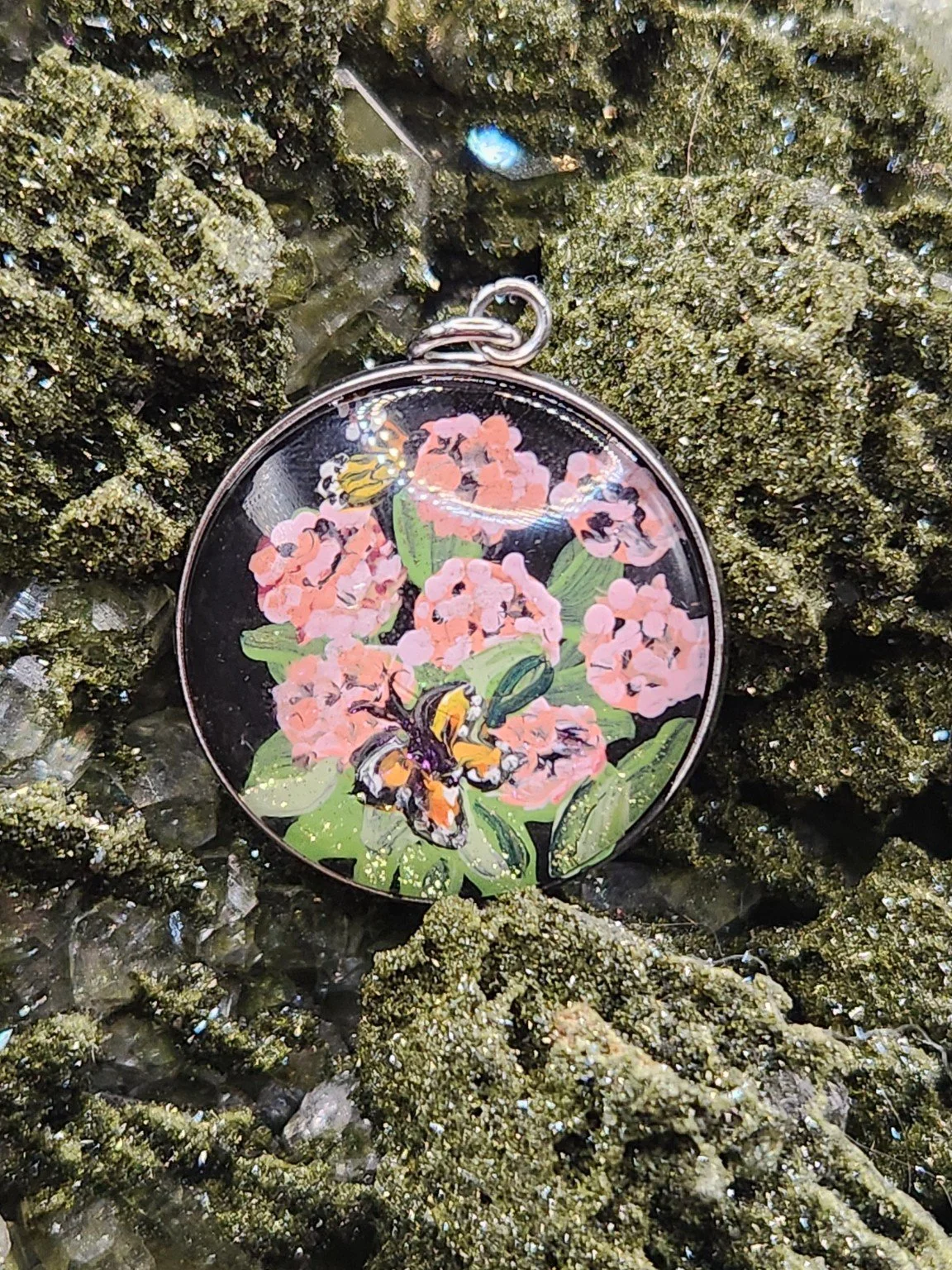 Pink milkweed and monarch butterfly art pendant nestled in a sparkling green crystal display. Crystal and display props not included.
