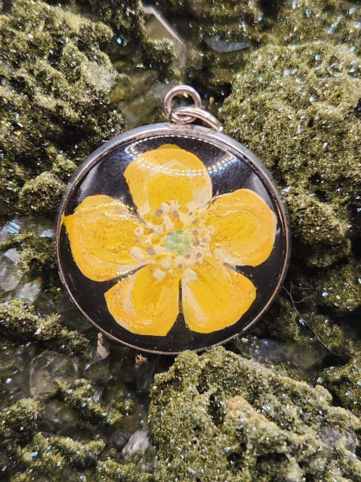 Golden yellow buttercup flower art pendant nestled in a sparkling green crystal display. Crystal and display props not included.