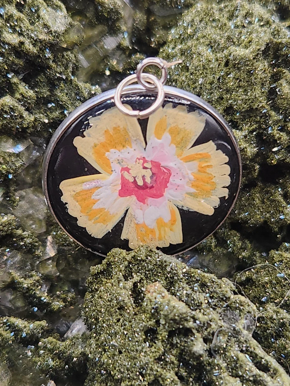 Yellow hibiscus flower art pendant resting on a green crystal display. Crystal display not included.