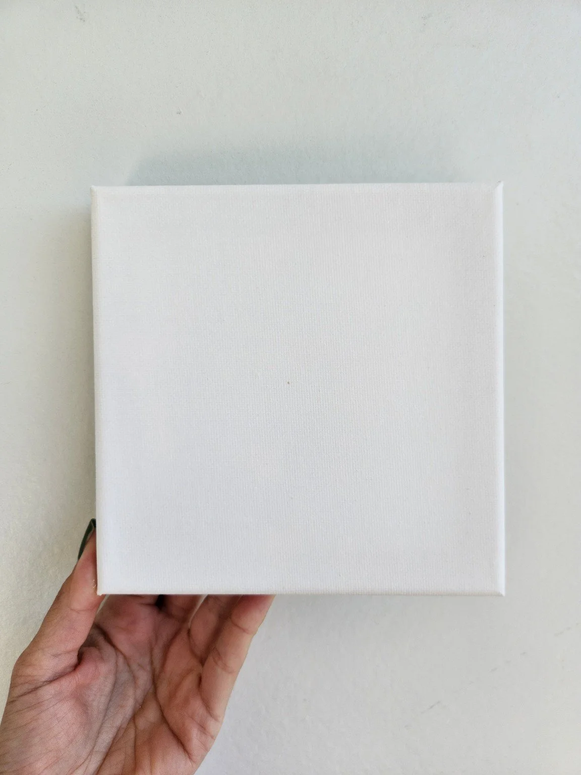 Blank square stretched canvas held in hand, showing the canvas format for a custom pet portrait.