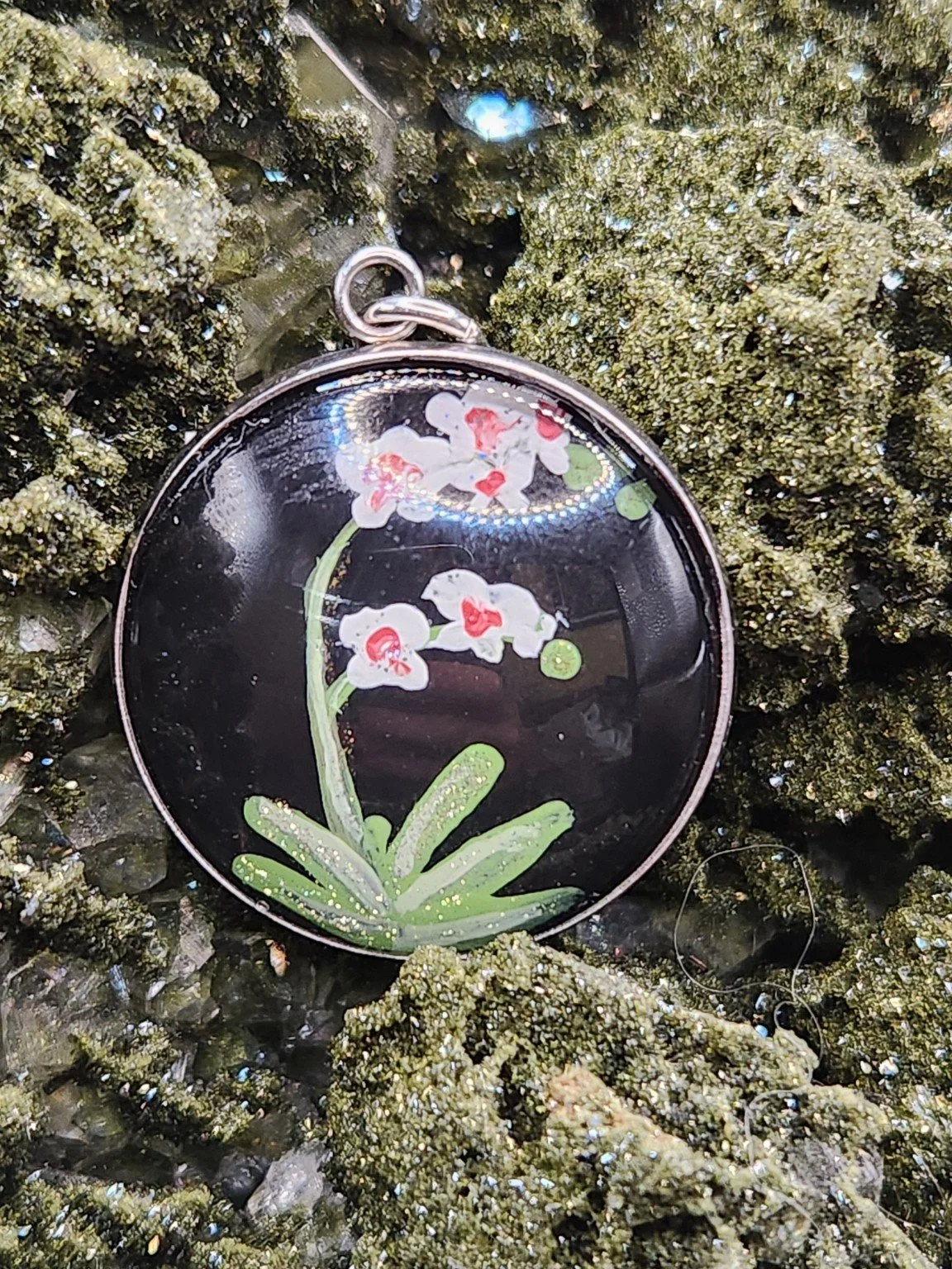 Orchid flower art pendant displayed among green crystals. Crystal display and props not included.