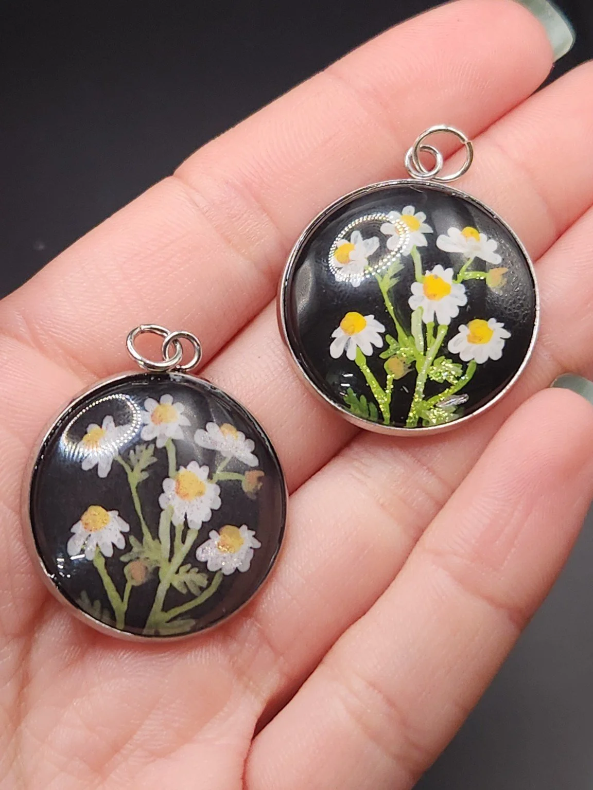 Chamomile pendant comparison held in a hand: the hand-painted original is at the top right, and the printed reproduction is at the bottom left.