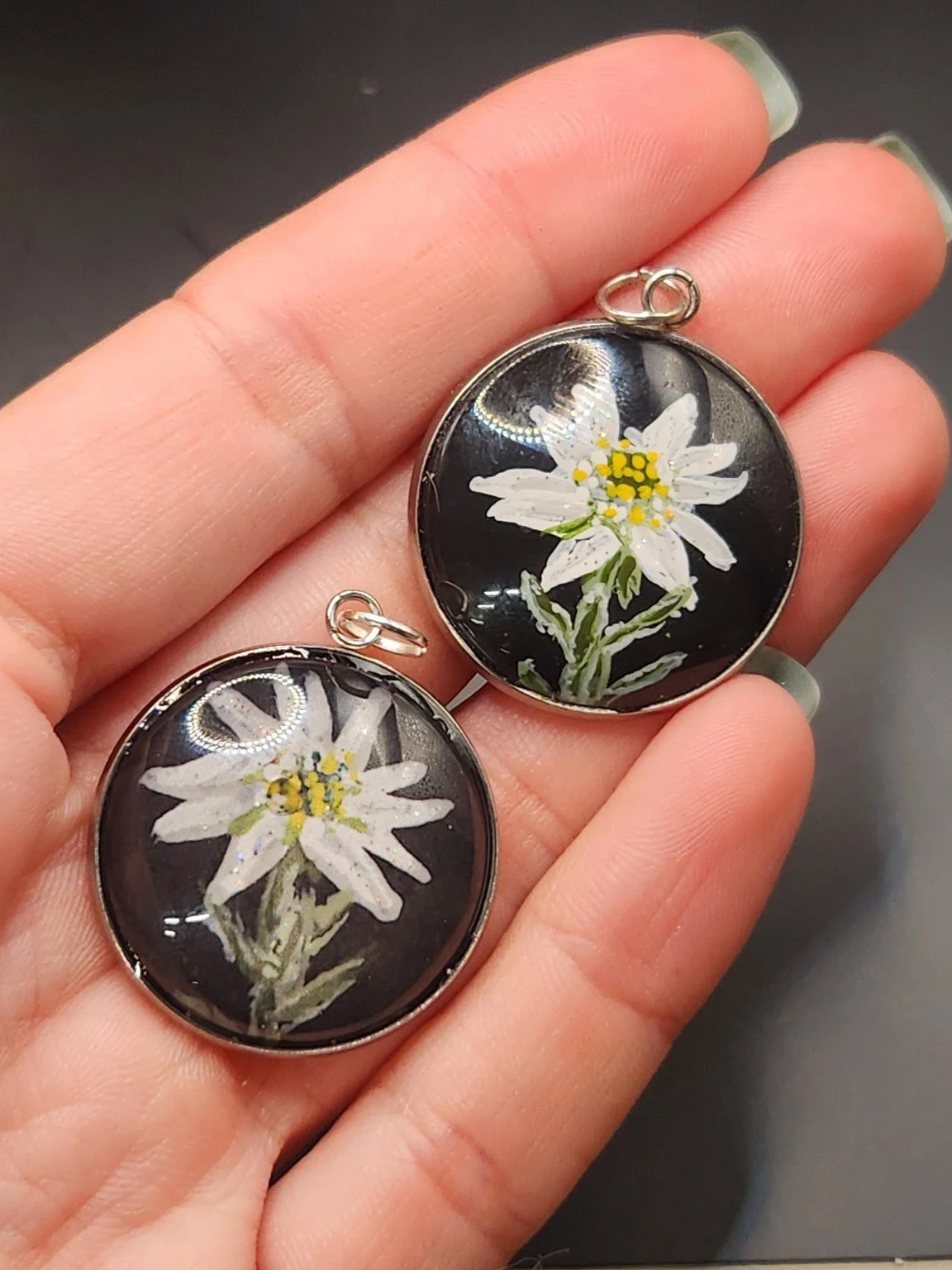 Edelweiss pendant comparison held in a hand: the hand-painted original is at the top right, and the printed reproduction is at the bottom left.