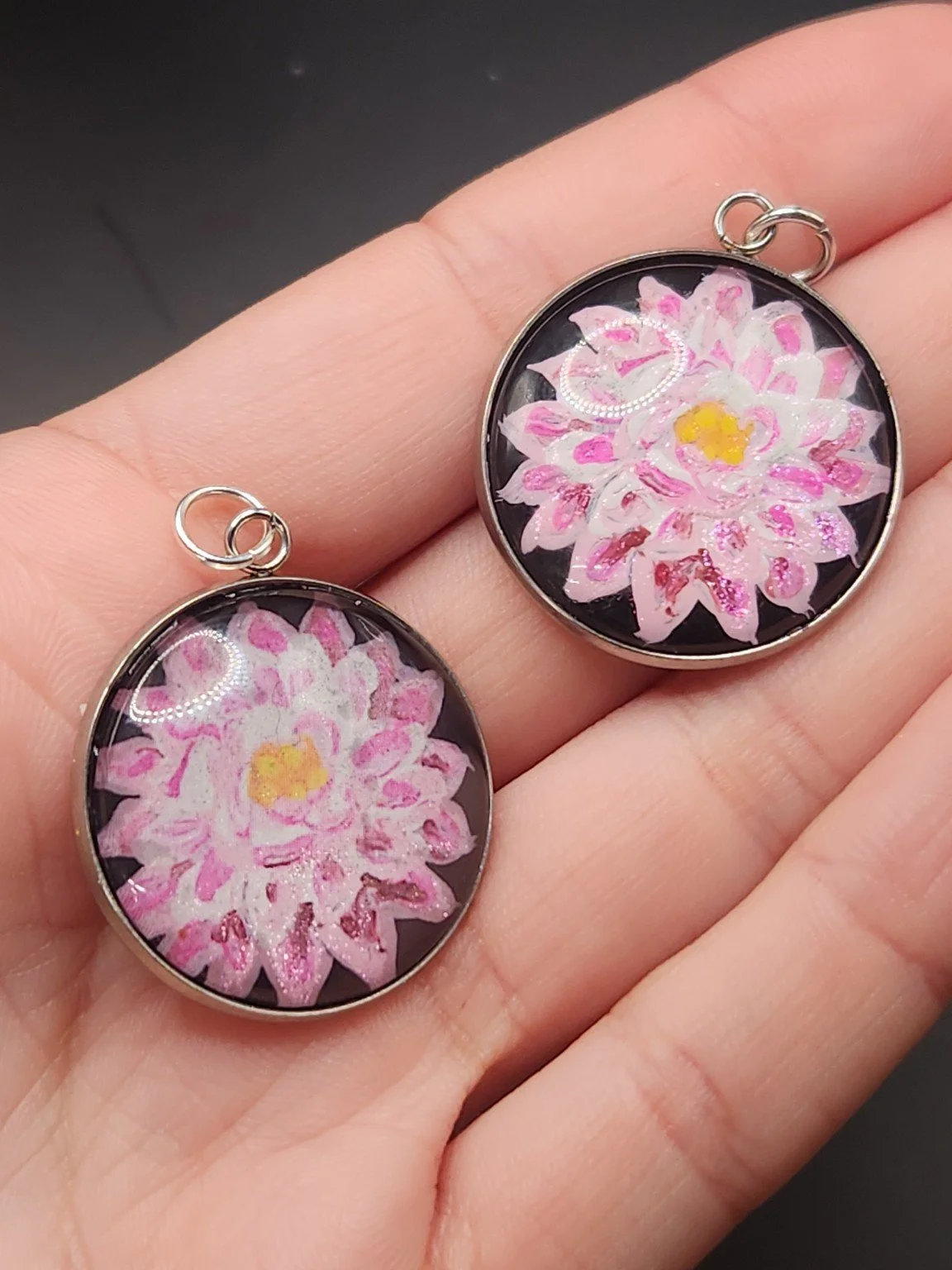 Dahlia pendant comparison held in a hand: the hand-painted original is at the top right, and the printed reproduction is at the bottom left.
