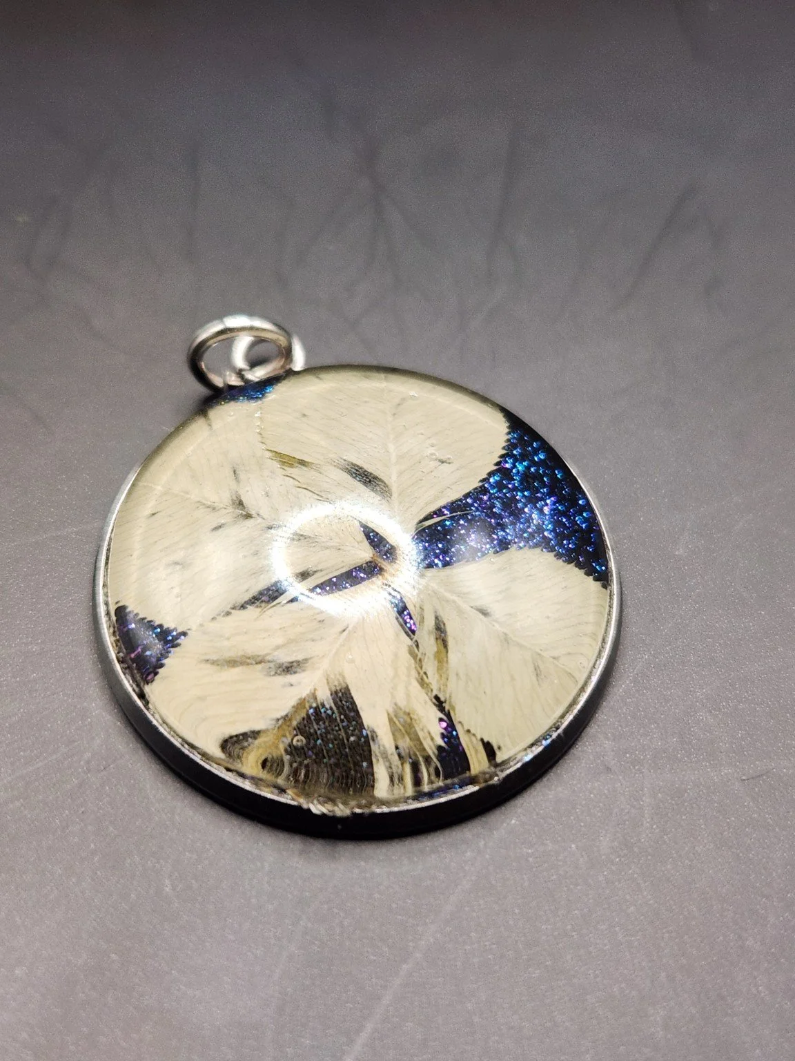 Naturally Unique N002: real pressed four-leaf clover pendant with blue glitter background, close-up on gray.