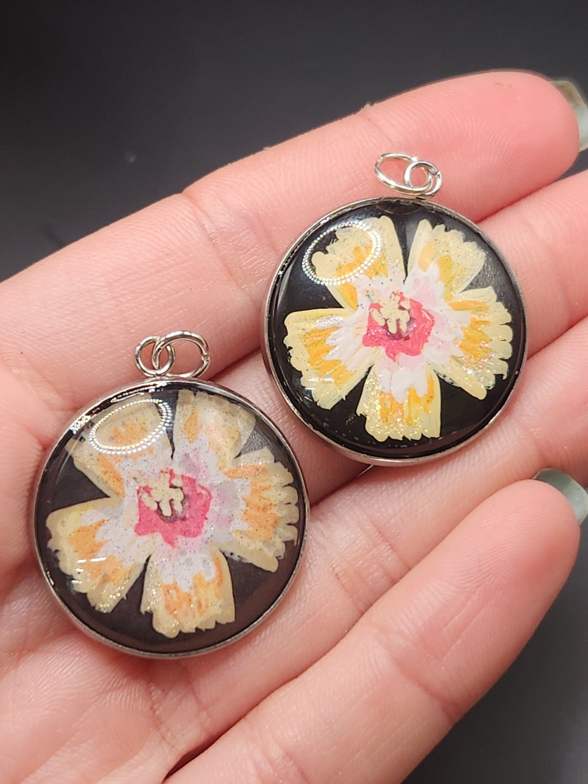 Hibiscus pendant comparison held in a hand: the hand-painted original is at the top right, and the printed reproduction is at the bottom left.