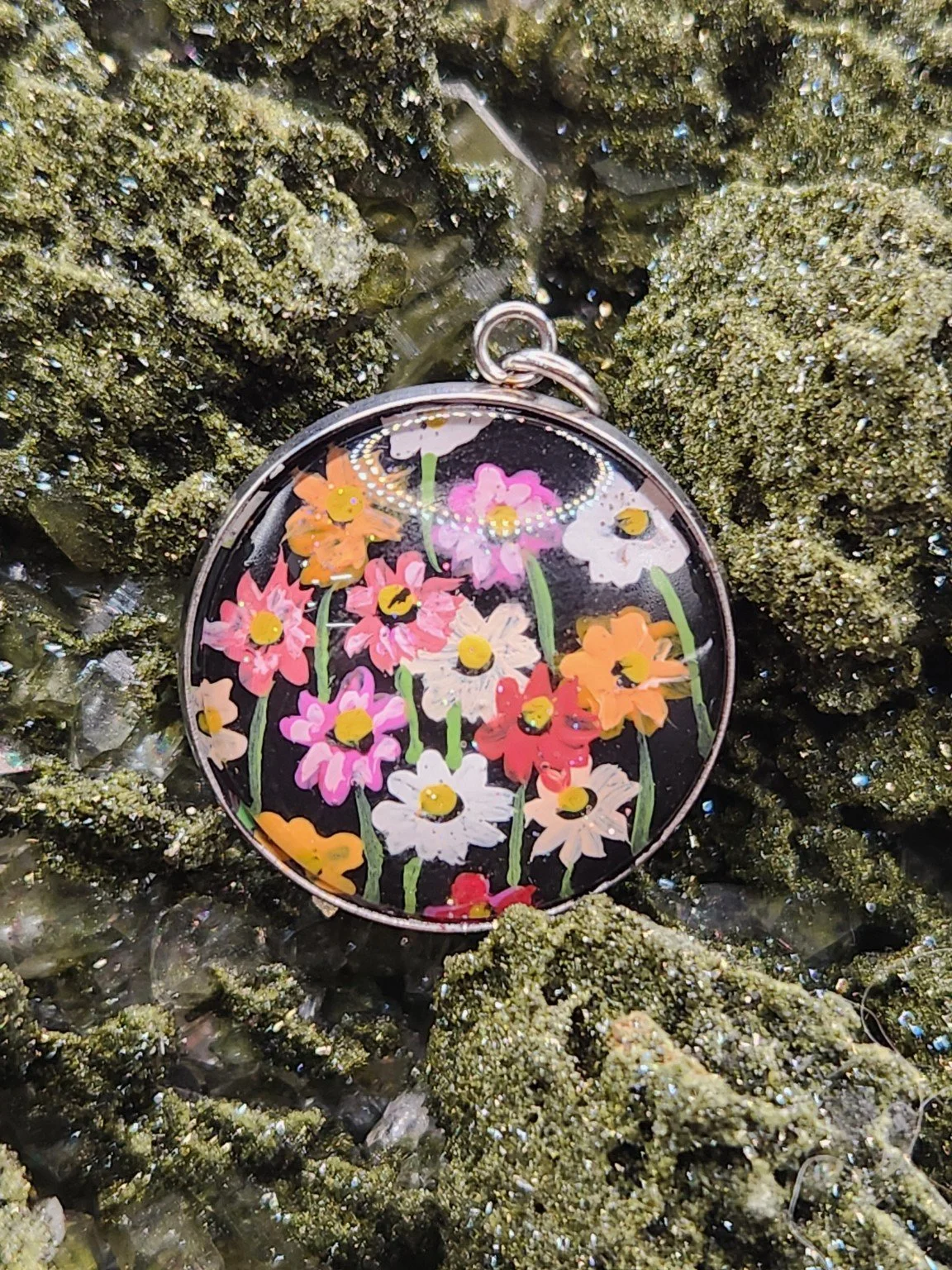 Cosmos flower art pendant displayed among green crystals. Crystal display and styling props not included.