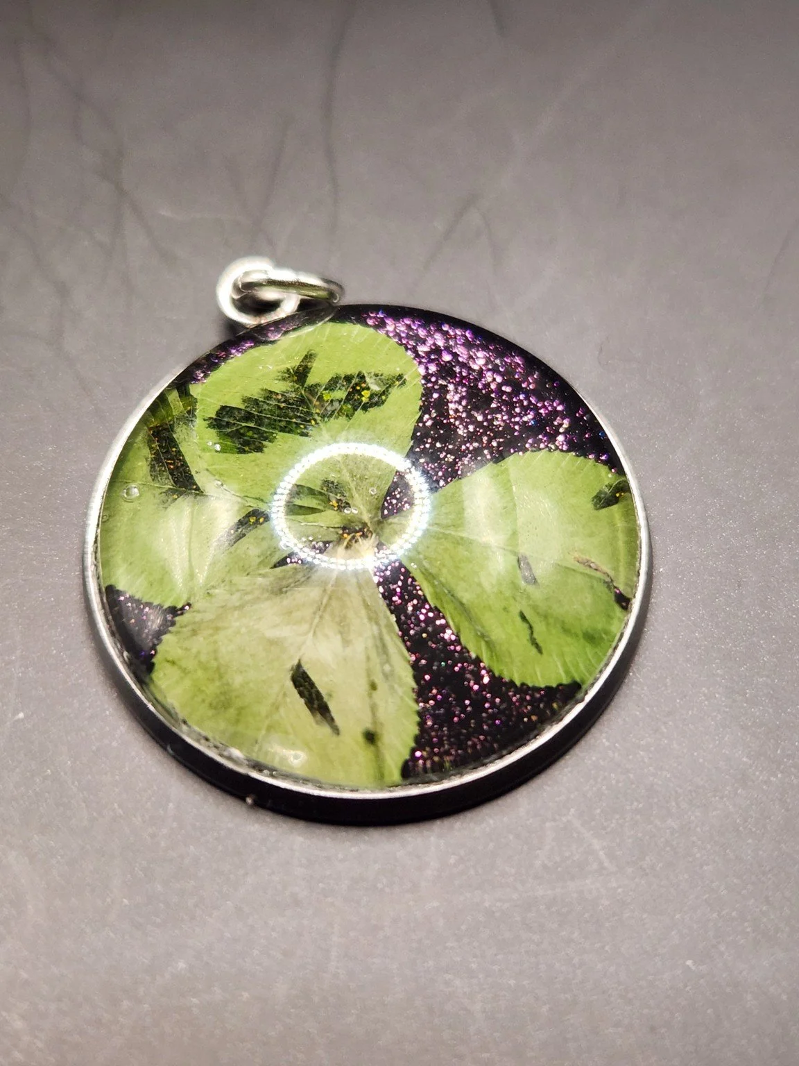 Naturally Unique N006: real pressed four-leaf clover pendant with purple glitter background, close-up on gray.