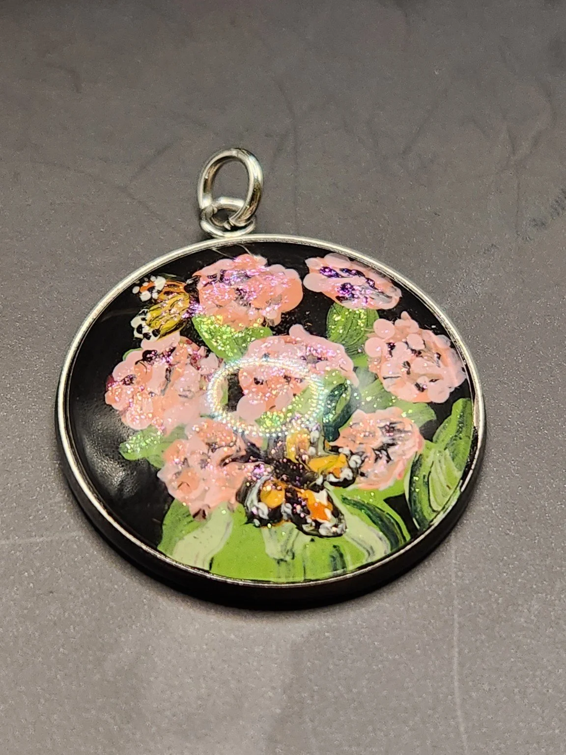 Milkweed flower art pendant with pink blossoms, green leaves, a monarch butterfly, and glitter accents in a silver-tone bezel.