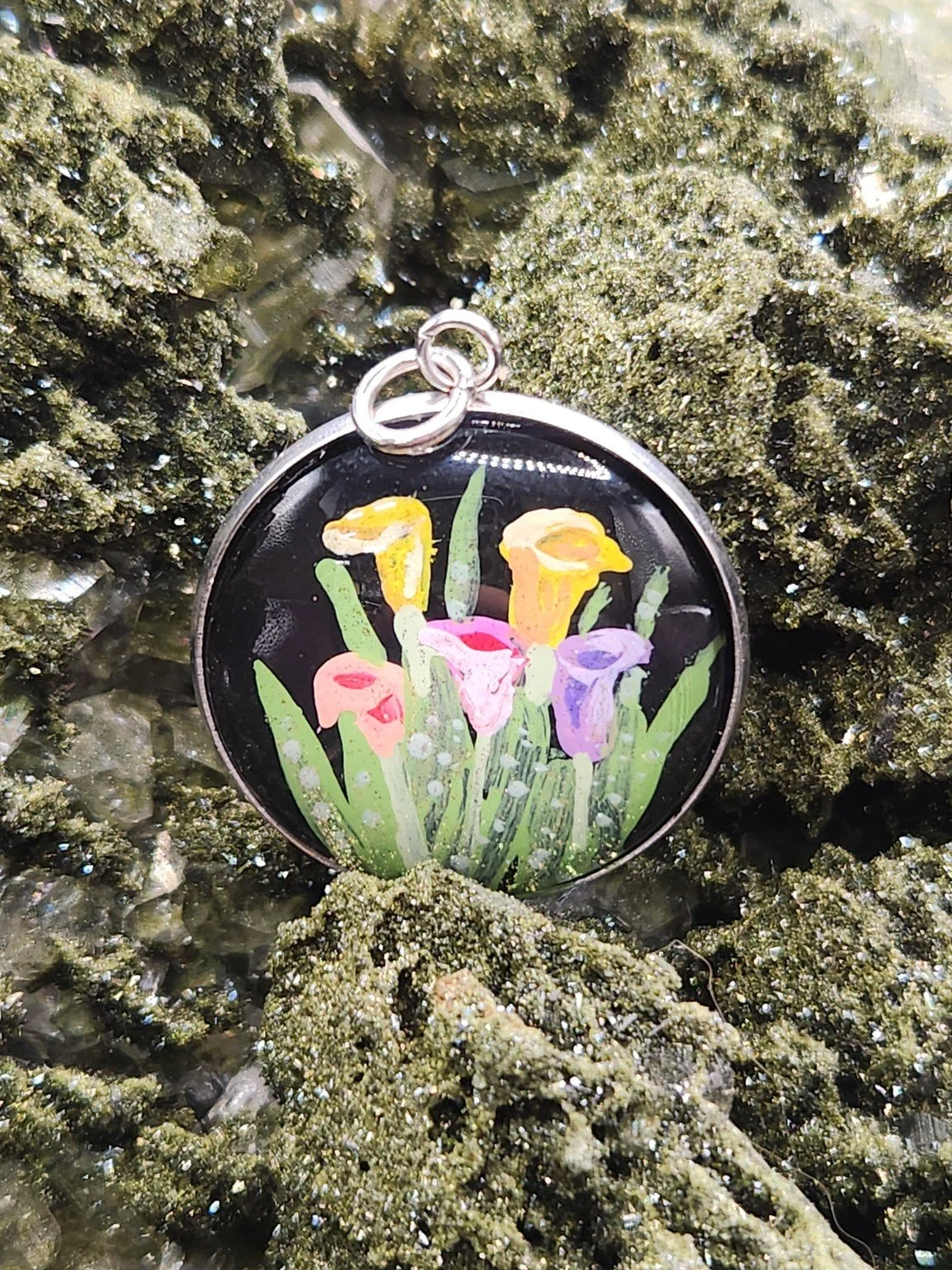Colorful calla lilies art pendant resting on a green crystal display. Crystal display not included.