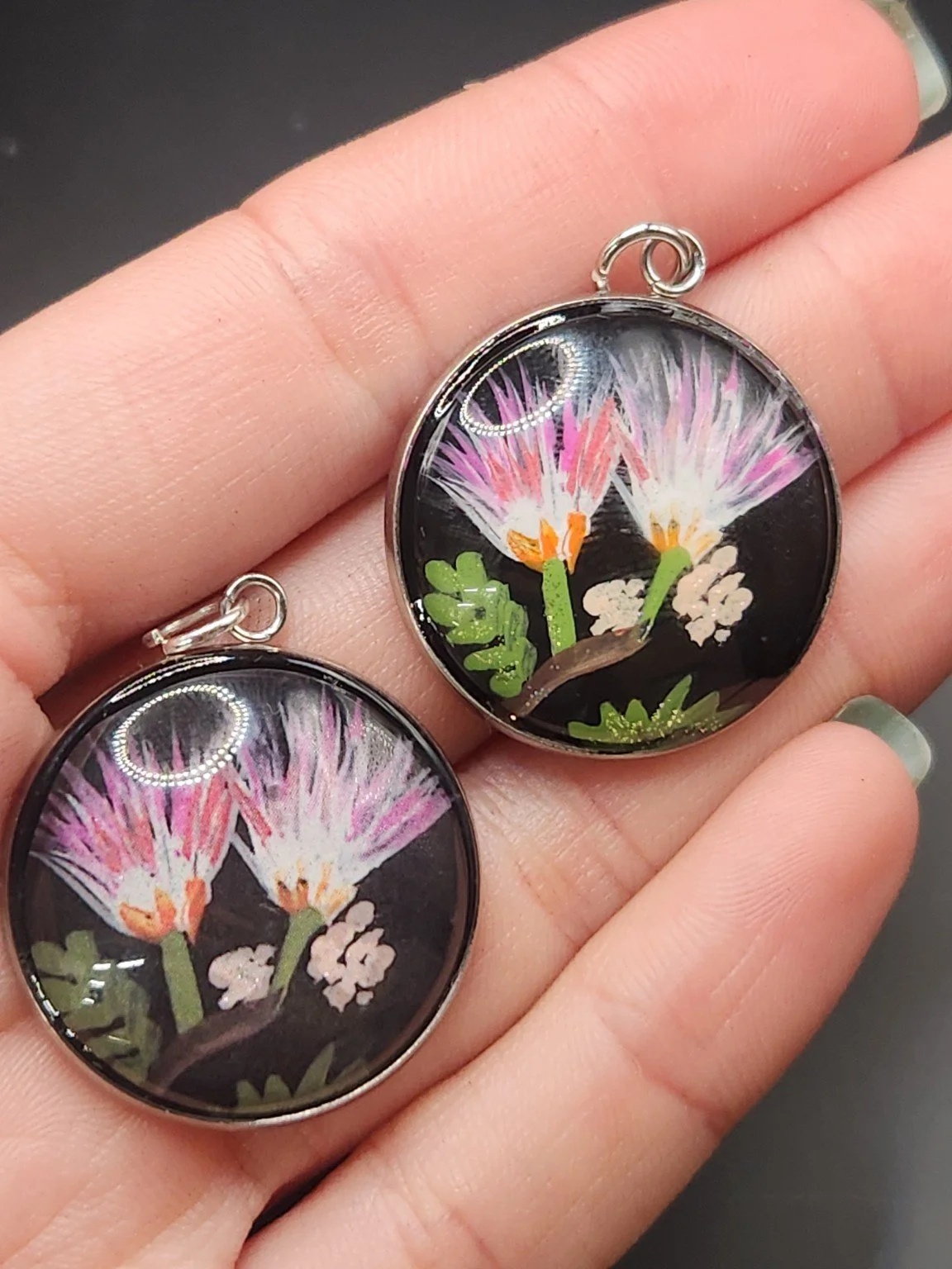 Mimosa pendant comparison held in a hand: the hand-painted original is at the top right, and the printed reproduction is at the bottom left.