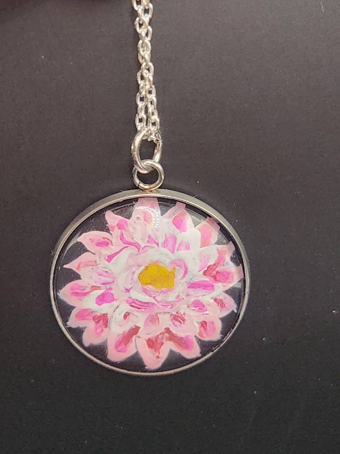 Pink dahlia flower art pendant shown on a silver-tone chain against a dark background. Chain not included.