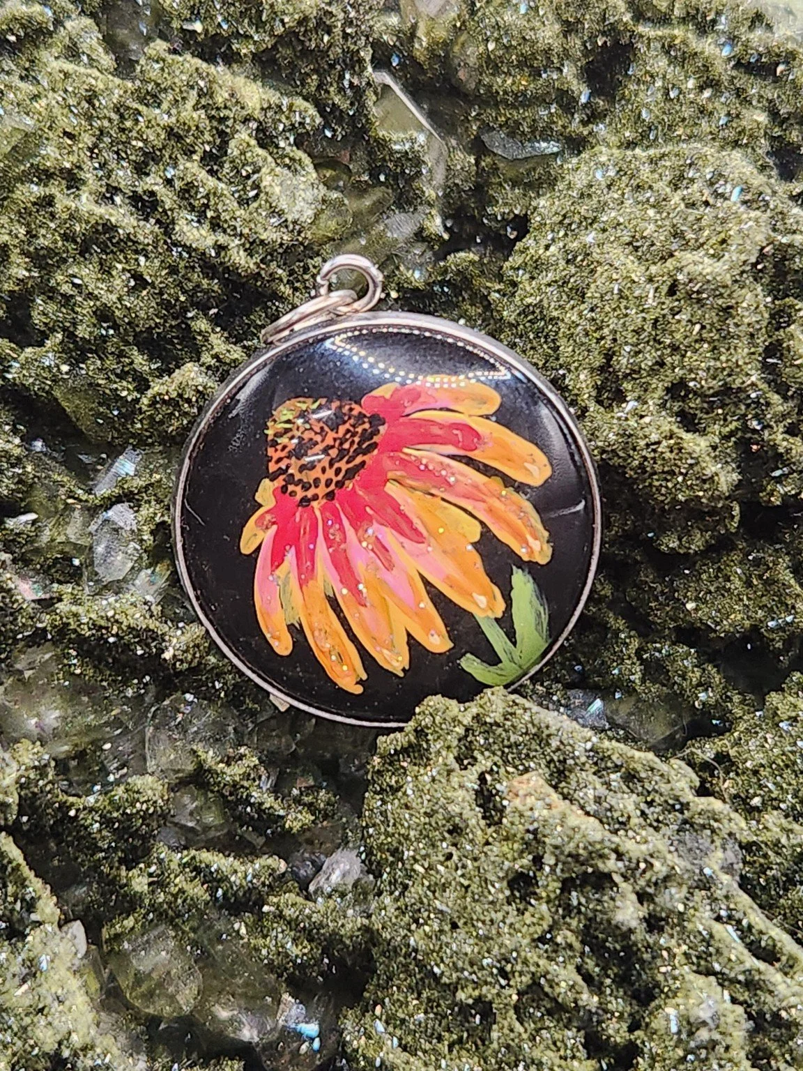 Red and yellow coneflower art pendant resting on a green crystal display. Crystal display not included.