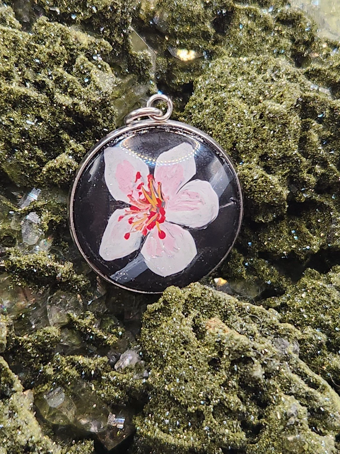 Pink cherry blossom art pendant nestled among green crystals. Crystal display and props not included.