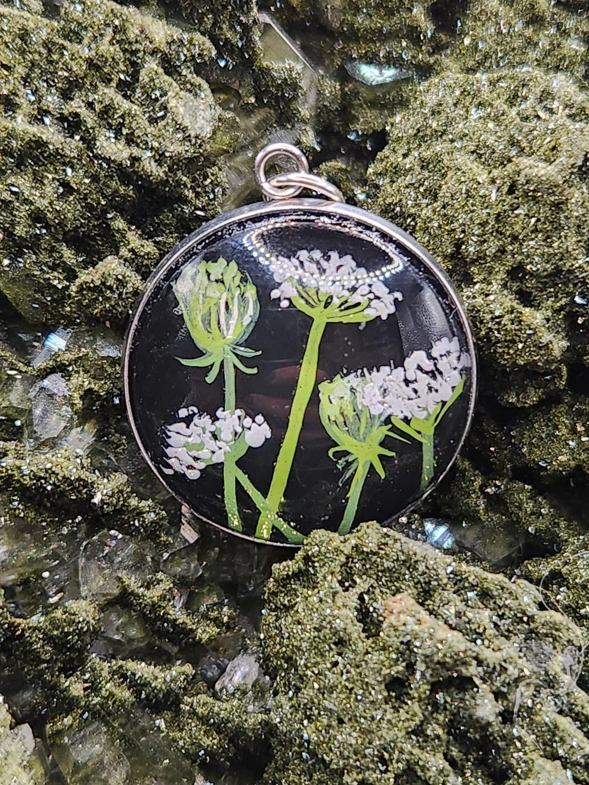 Queen Anne’s lace flower art pendant resting on a green crystal display. Crystal display not included.