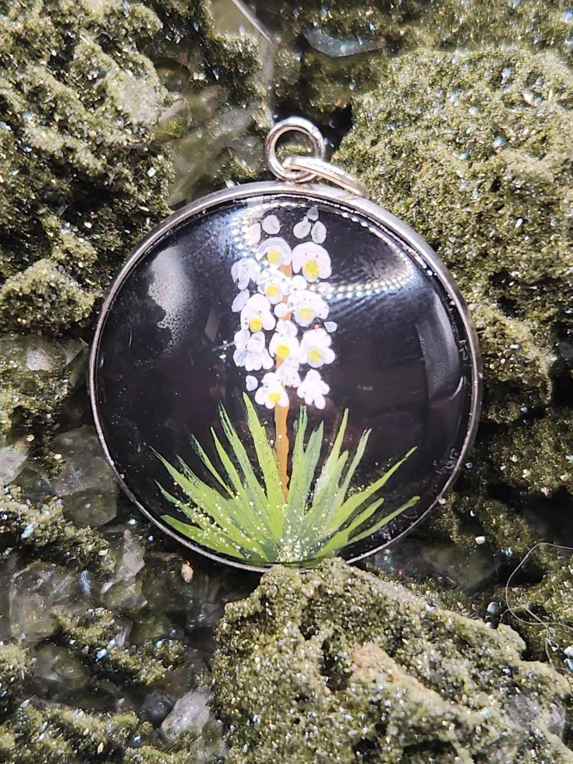 Yucca flower art pendant displayed among green crystals. Crystal display and styling props not included.