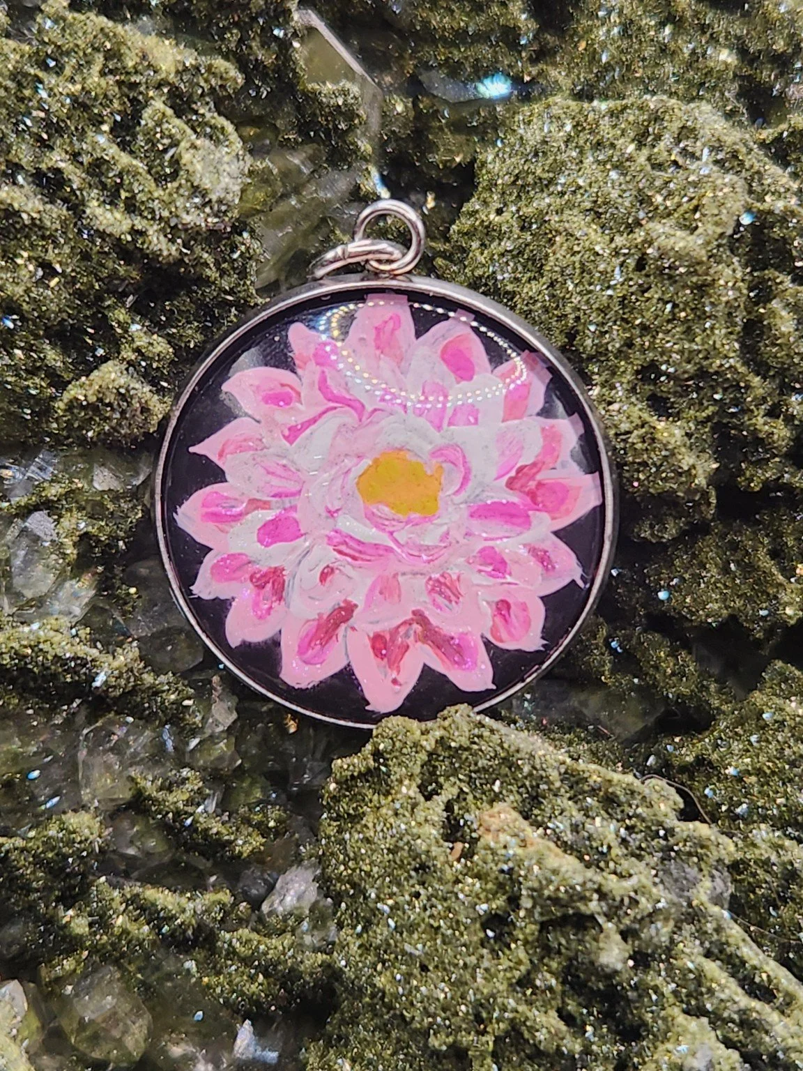 Pink dahlia flower art pendant resting on a green crystal display. Crystal display not included.