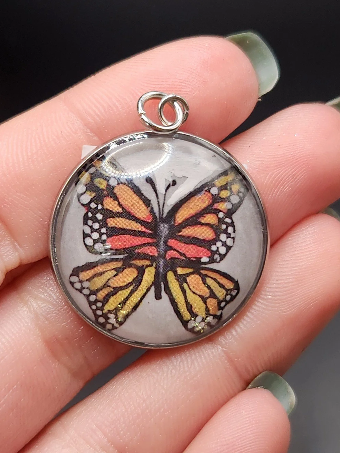 Discounted imperfect monarch butterfly print pendant held in a hand. This is the $20 misprint option, separate from the hand-painted original.