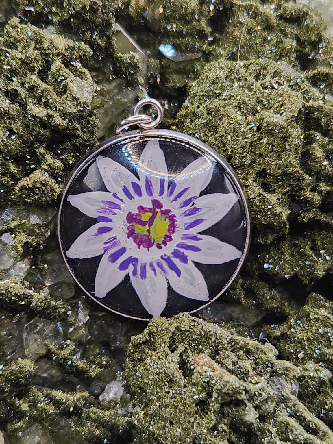 Purple and white passion flower art pendant nestled in a sparkling green crystal display. Crystal and display props not included.