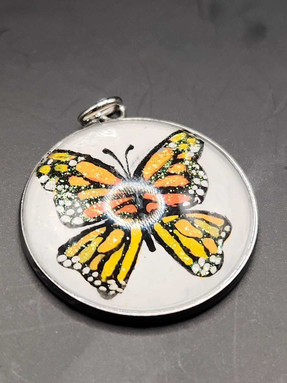 Hand-painted monarch butterfly art pendant with orange and black wings, white spots, and glitter accents in a silver-tone bezel.