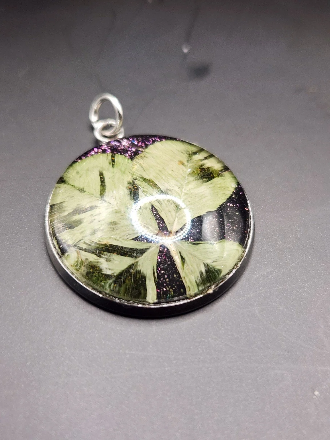 Perfectly Imperfect I001: real four-leaf clover pendant with purple glitter and distinctive translucent leaf patterns, close-up on gray.