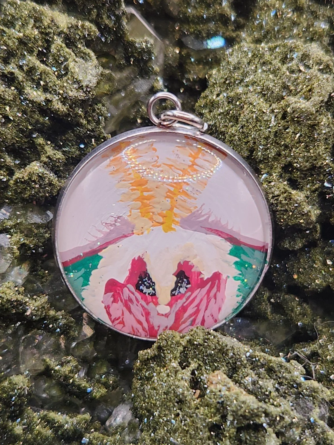 White-background hand-painted luna moth face original pendant resting on a green crystal display. Crystal display not included.