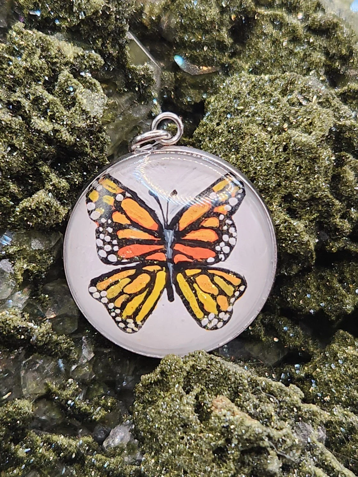 Hand-painted monarch butterfly art pendant nestled in a sparkling green crystal display. Crystal and display props not included.