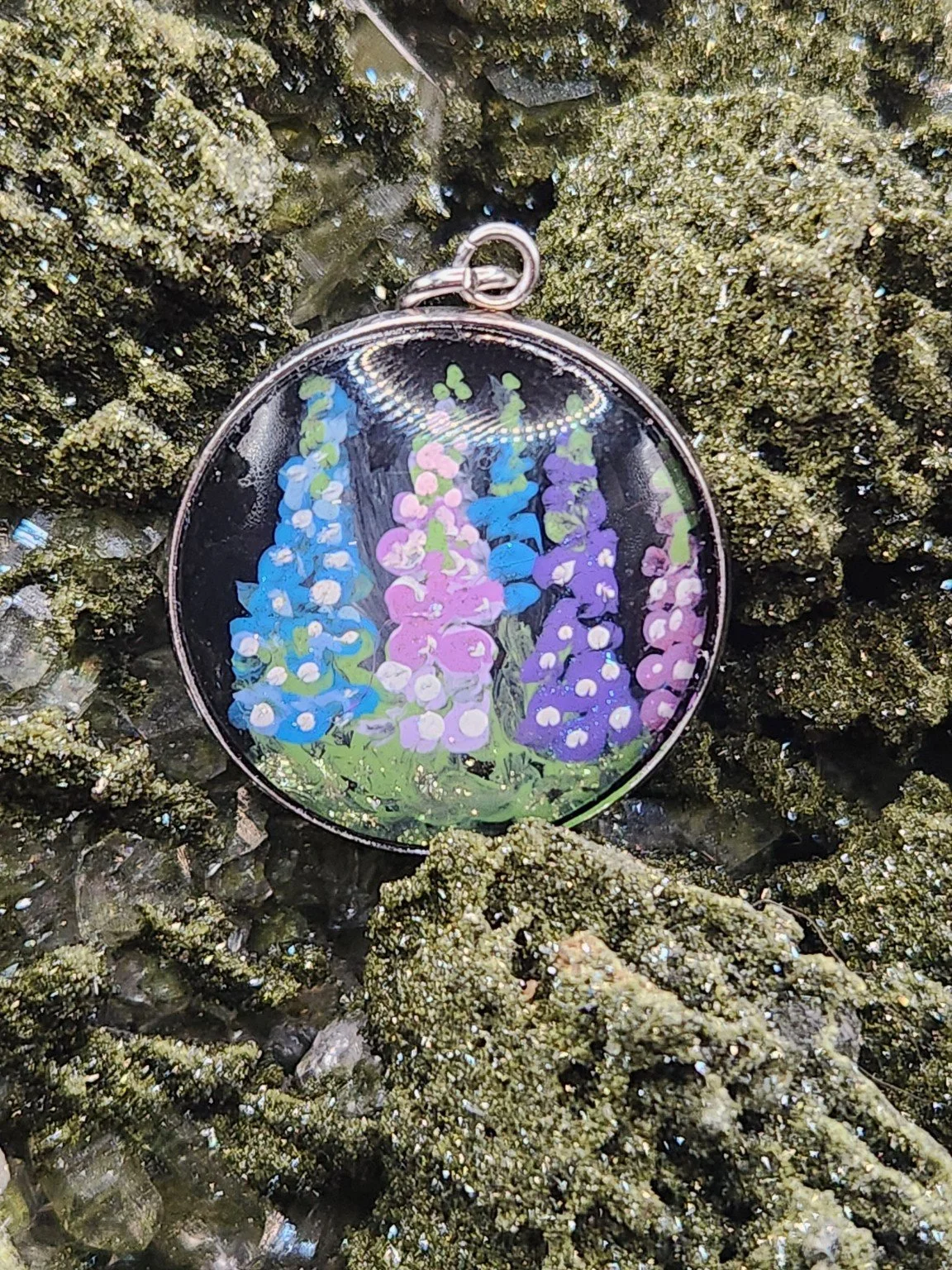 Colorful delphinium flower art pendant resting on a green crystal display. Crystal display not included.