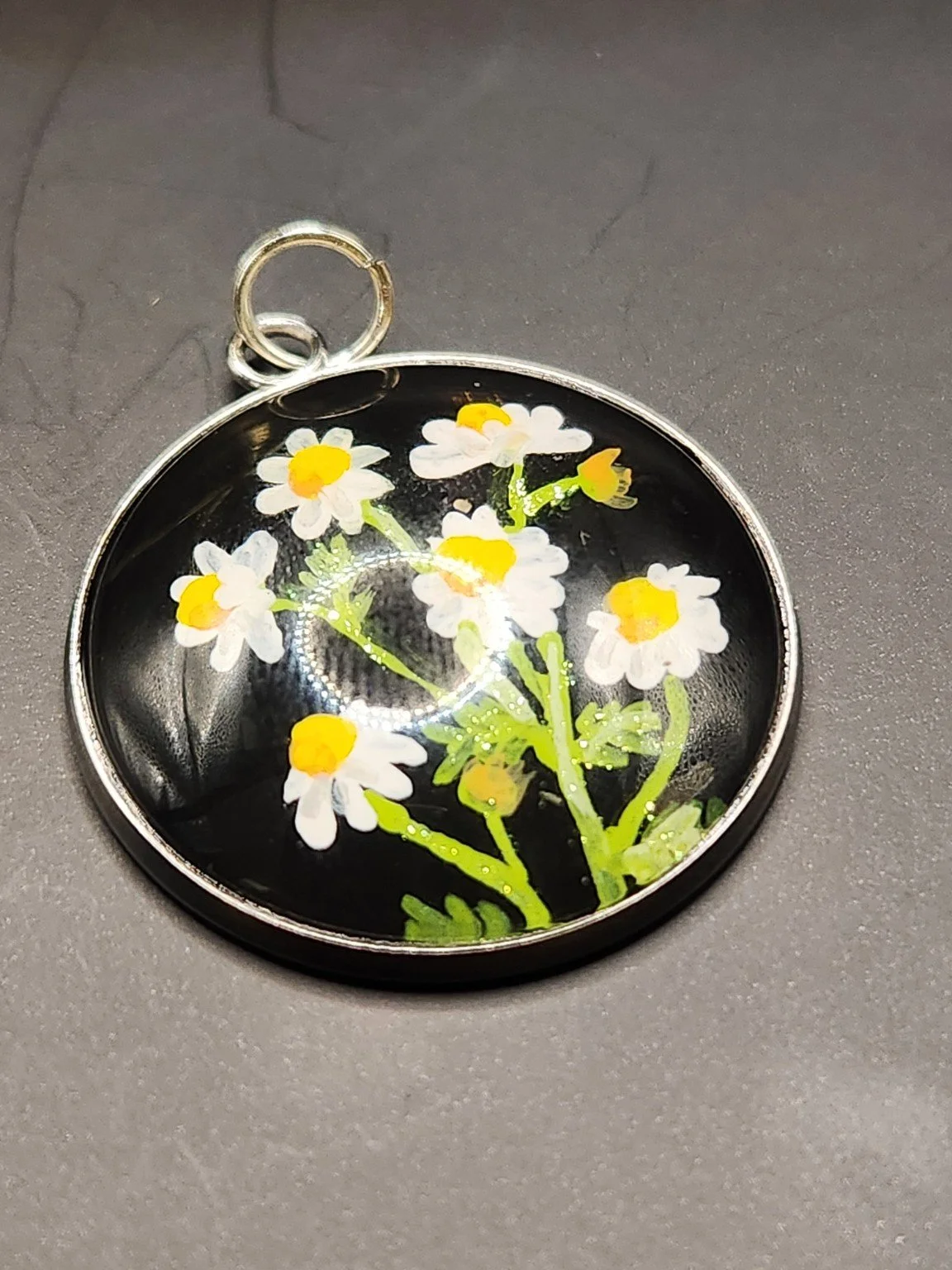 Chamomile art pendant with white petals, yellow centers, and green stems, showing the glitter finish on a gray background.
