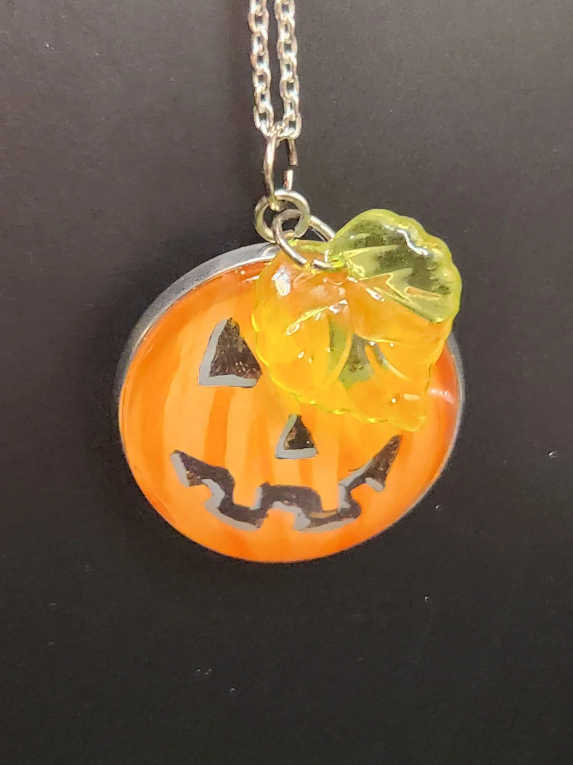 Original jack-o-lantern pumpkin art pendant with leaf charm hanging from a chain. Chain not included.