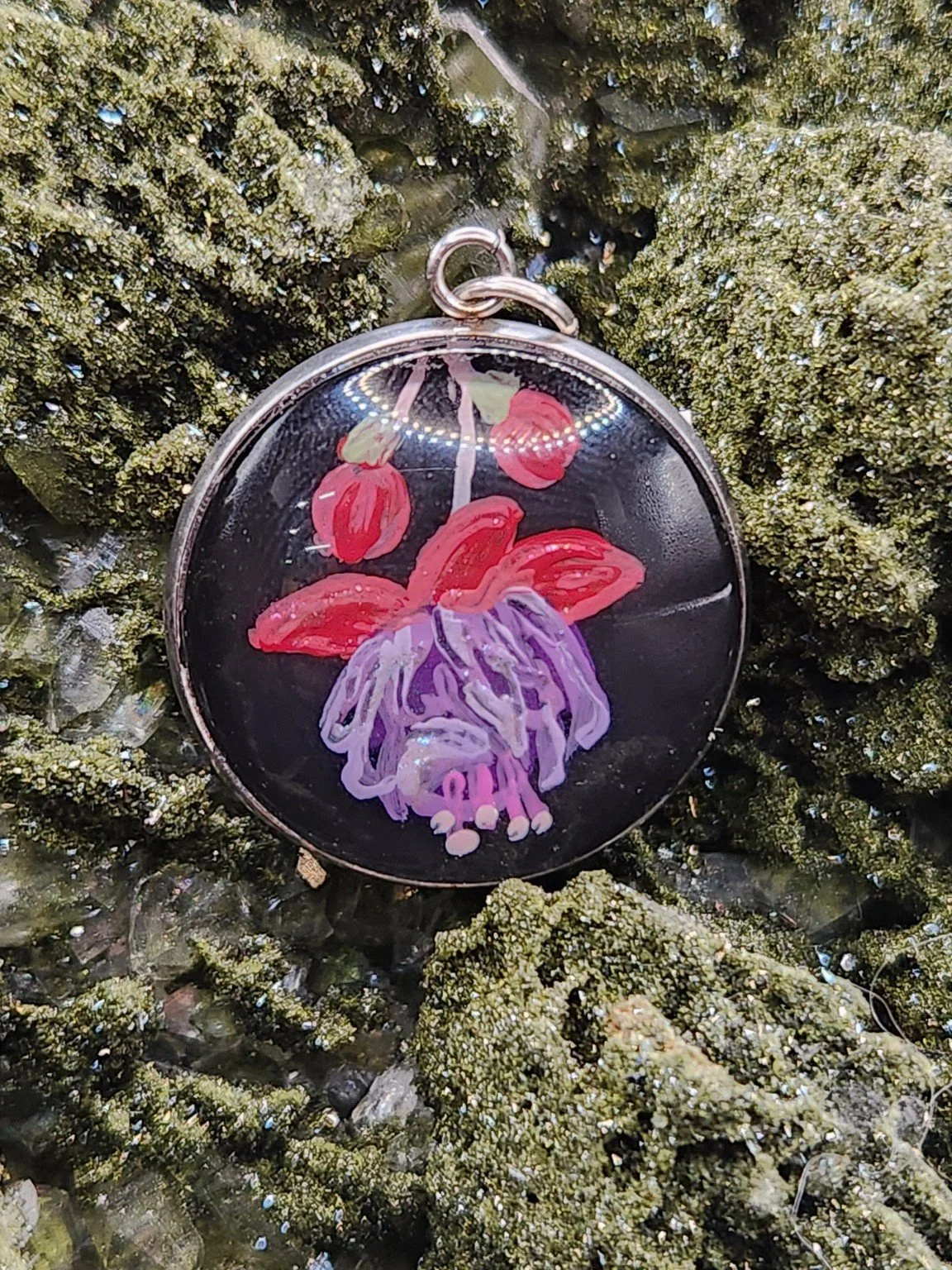 Fuchsia flower art pendant displayed among green crystals. Crystal display and styling props not included.