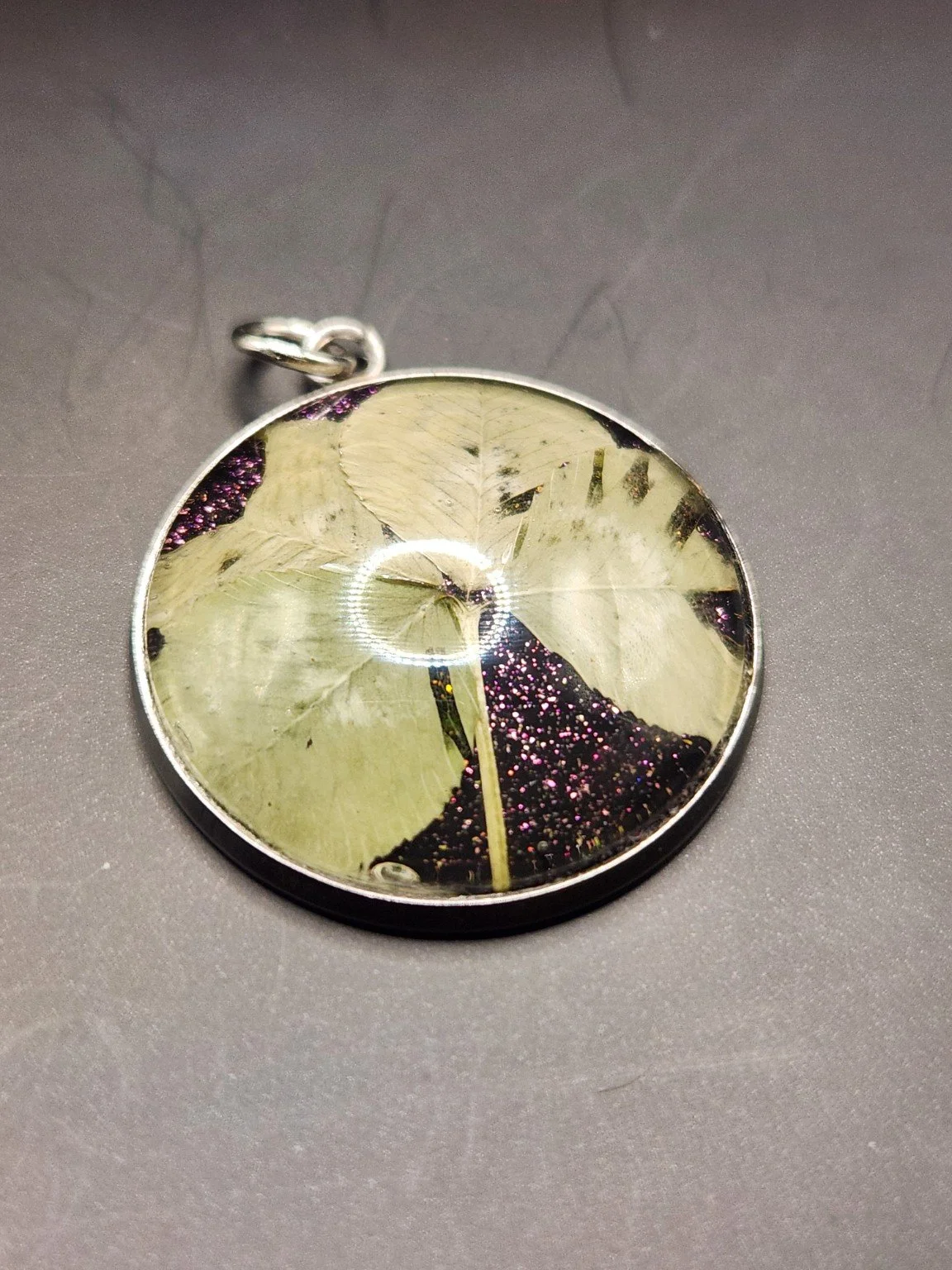 Naturally Unique N001: real pressed four-leaf clover pendant with purple glitter background, close-up on gray.