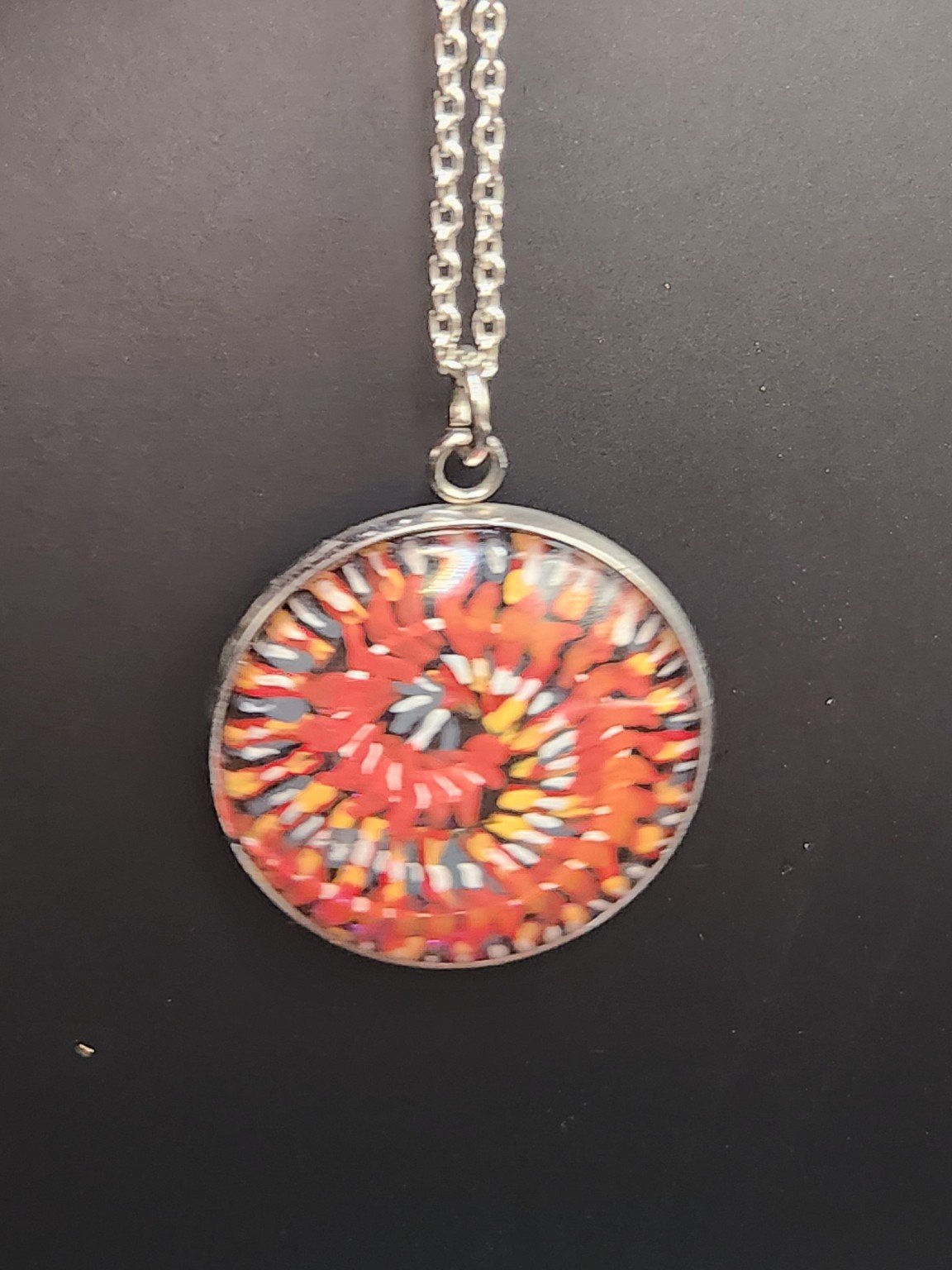 Coiled red-and-orange Millipede Design 1 art pendant shown on a silver-tone chain against a dark background. Chain not included.