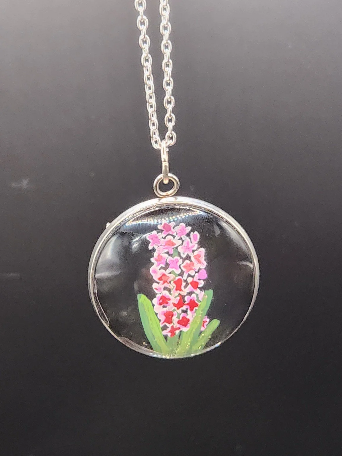 Pink hyacinth flower art pendant hanging from a silver-tone chain against a dark background. Chain not included.