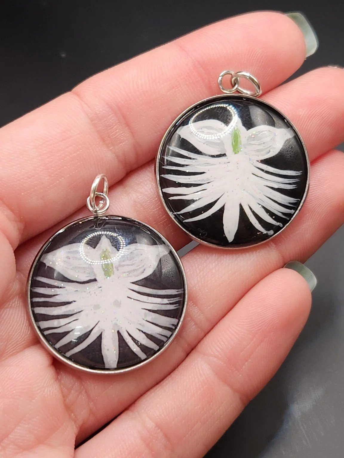 Two dove orchid flower pendants in a hand: hand-painted original at the top right and printed reproduction at the bottom left.