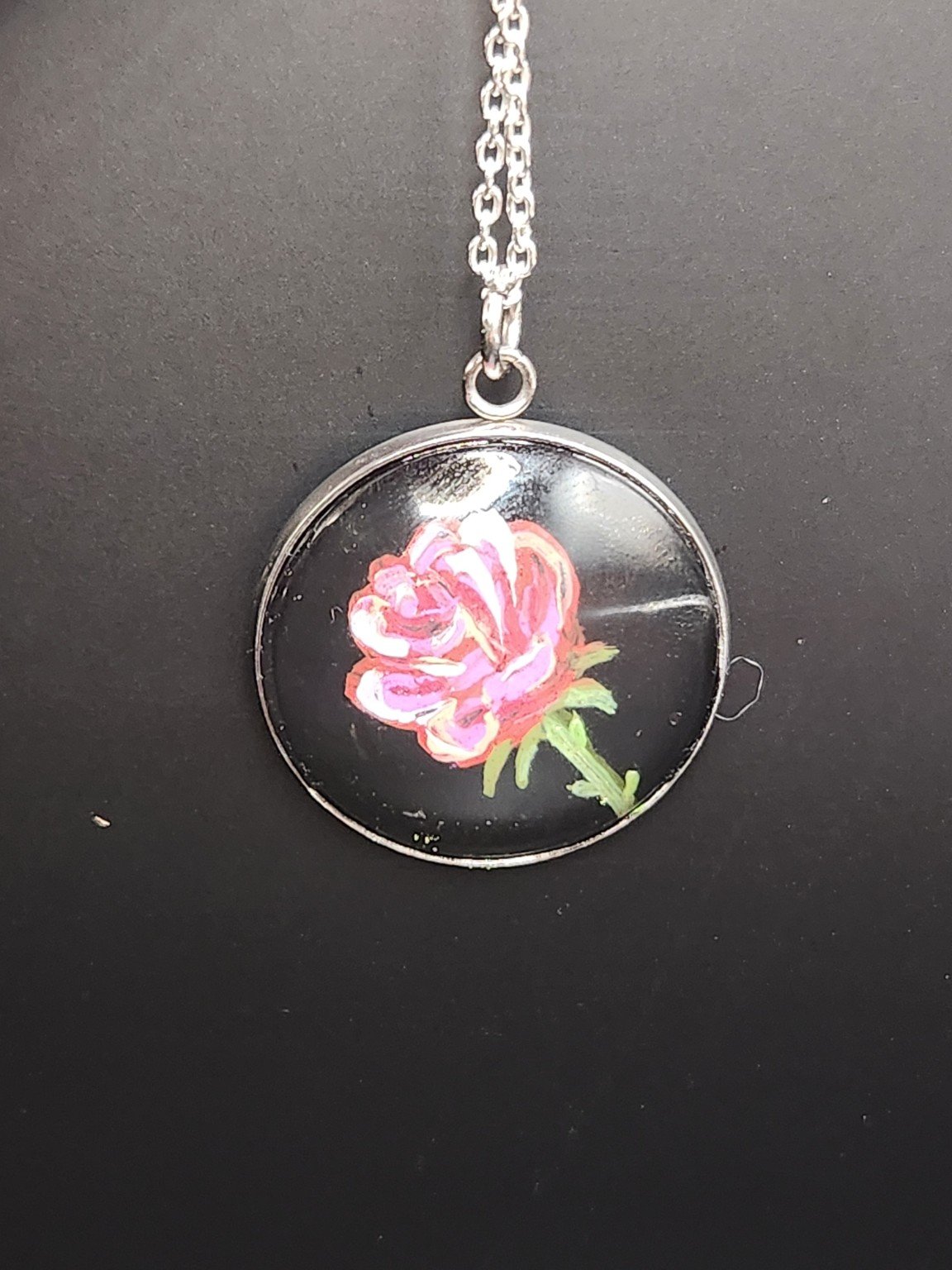 Pink rose art pendant shown on a silver-tone chain against a dark background. Chain not included.