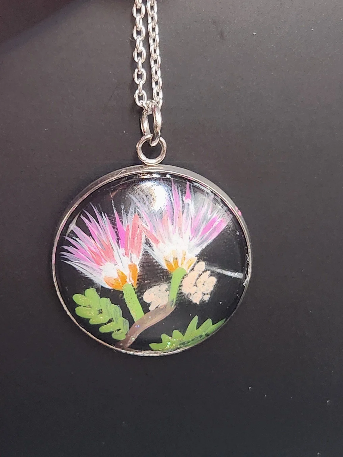 Pink mimosa flower art pendant shown on a silver-tone chain against a dark background. Chain not included.
