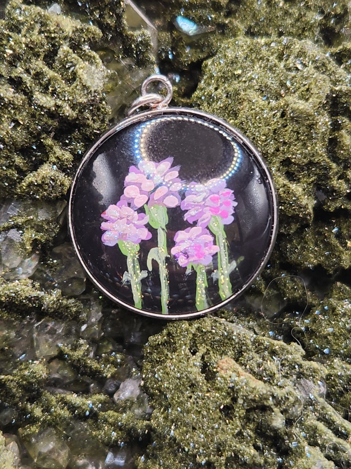 Pink and purple carnation flower art pendant resting on a green crystal display. Crystal display not included.