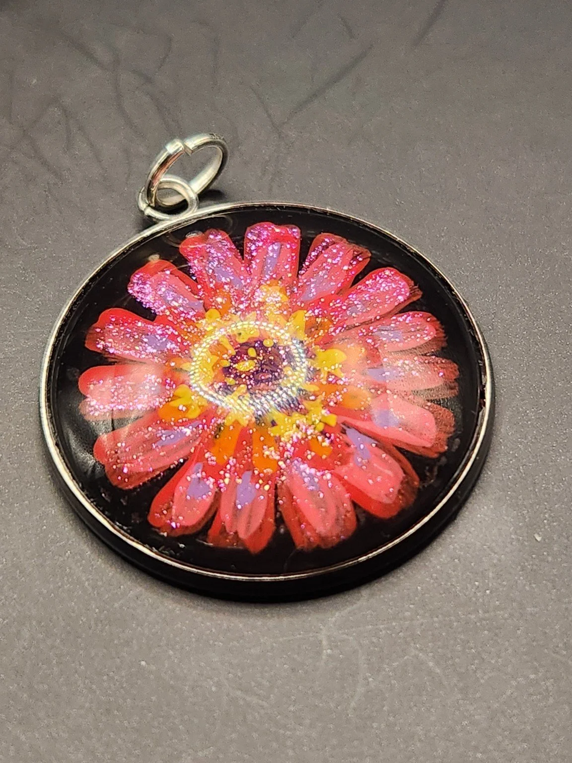 Zinnia flower art pendant with glitter, shown close up.