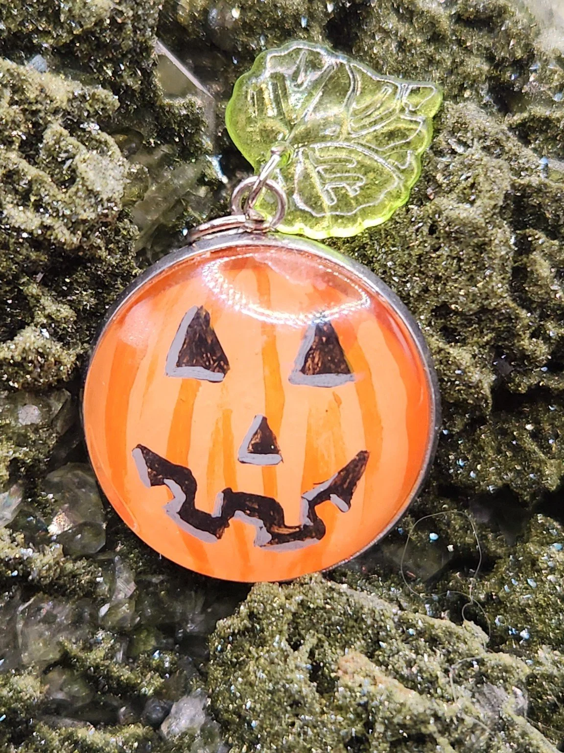 Original pumpkin art pendant displayed among green crystals. Crystal display and props not included.