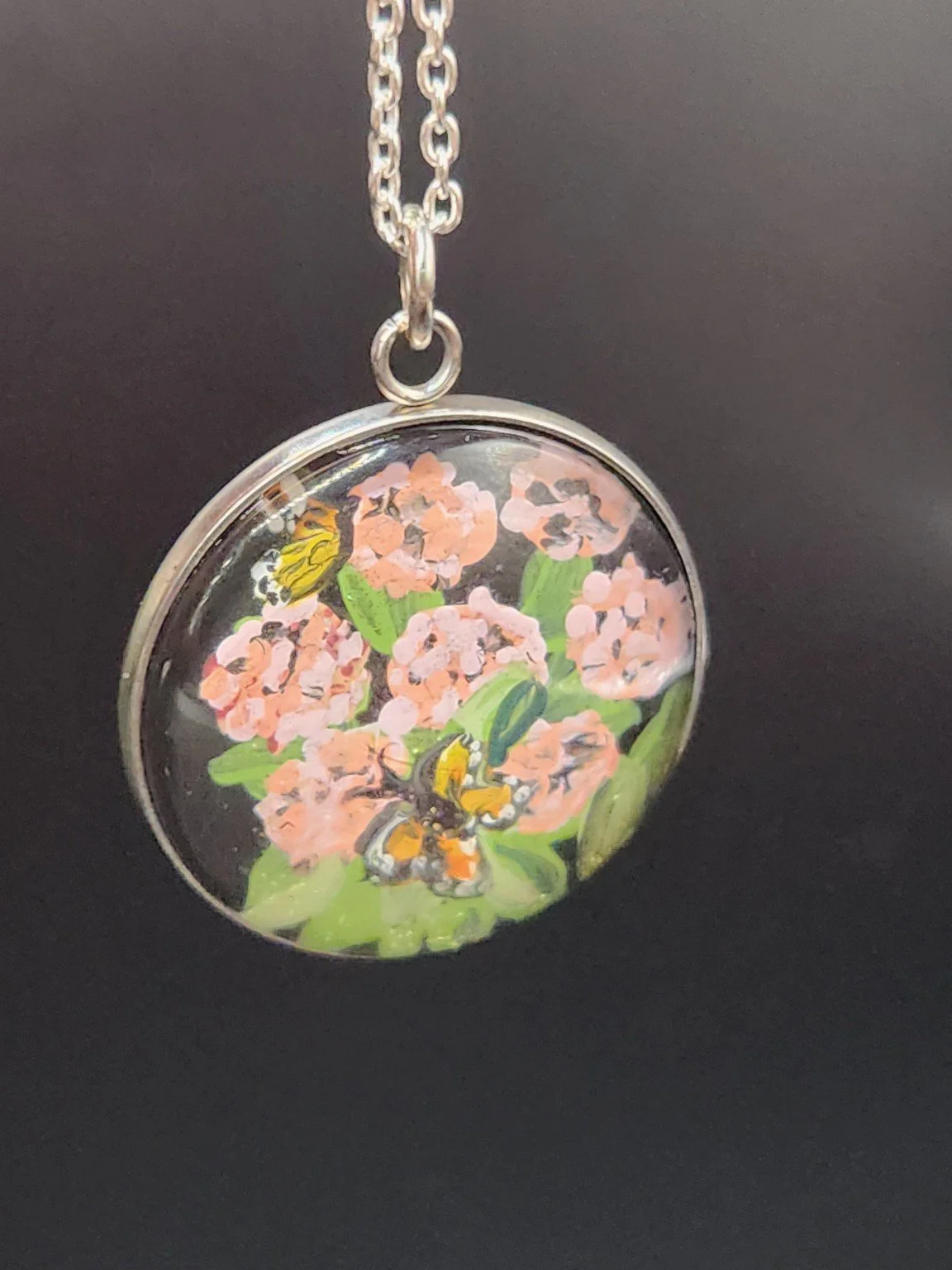 Pink milkweed and monarch butterfly art pendant hanging from a silver-tone chain against a dark background. Chain not included.