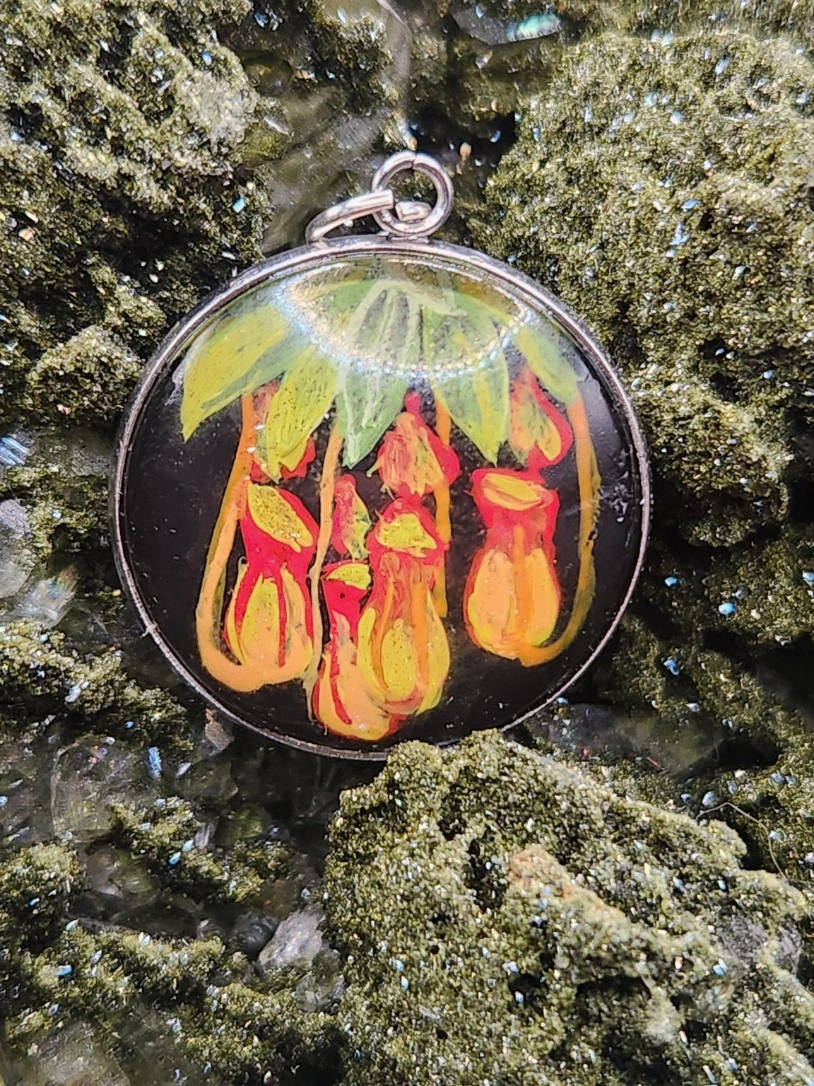 Pitcher plant art pendant resting on a green crystal display. Crystal display not included.