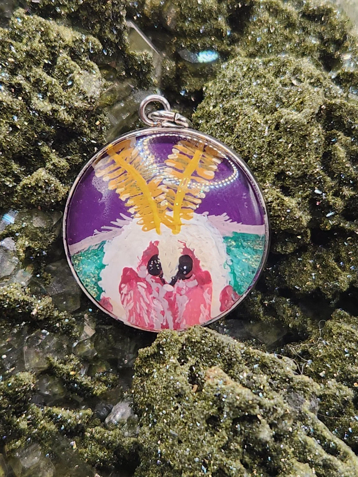 Purple-background hand-painted luna moth face original pendant resting on a green crystal display. Crystal display not included.