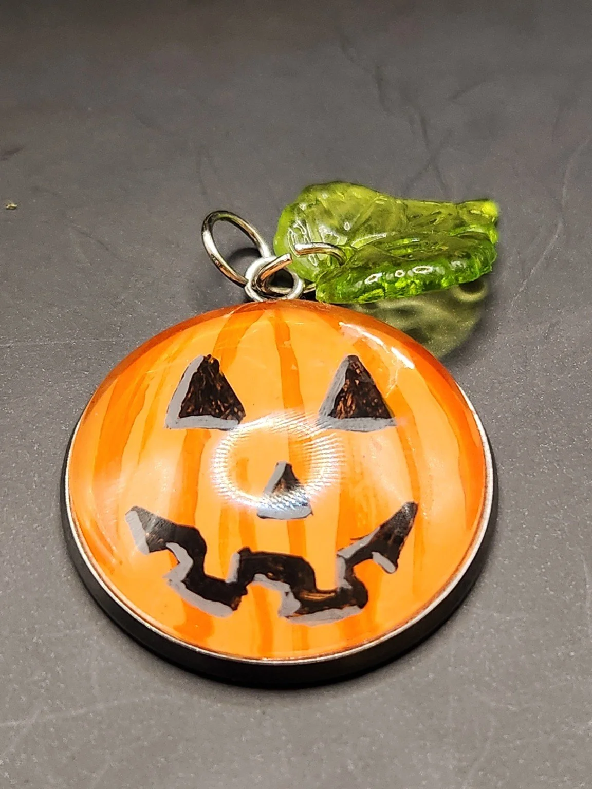 Hand-painted orange jack-o-lantern pumpkin pendant with glitter accents and a green leaf charm.