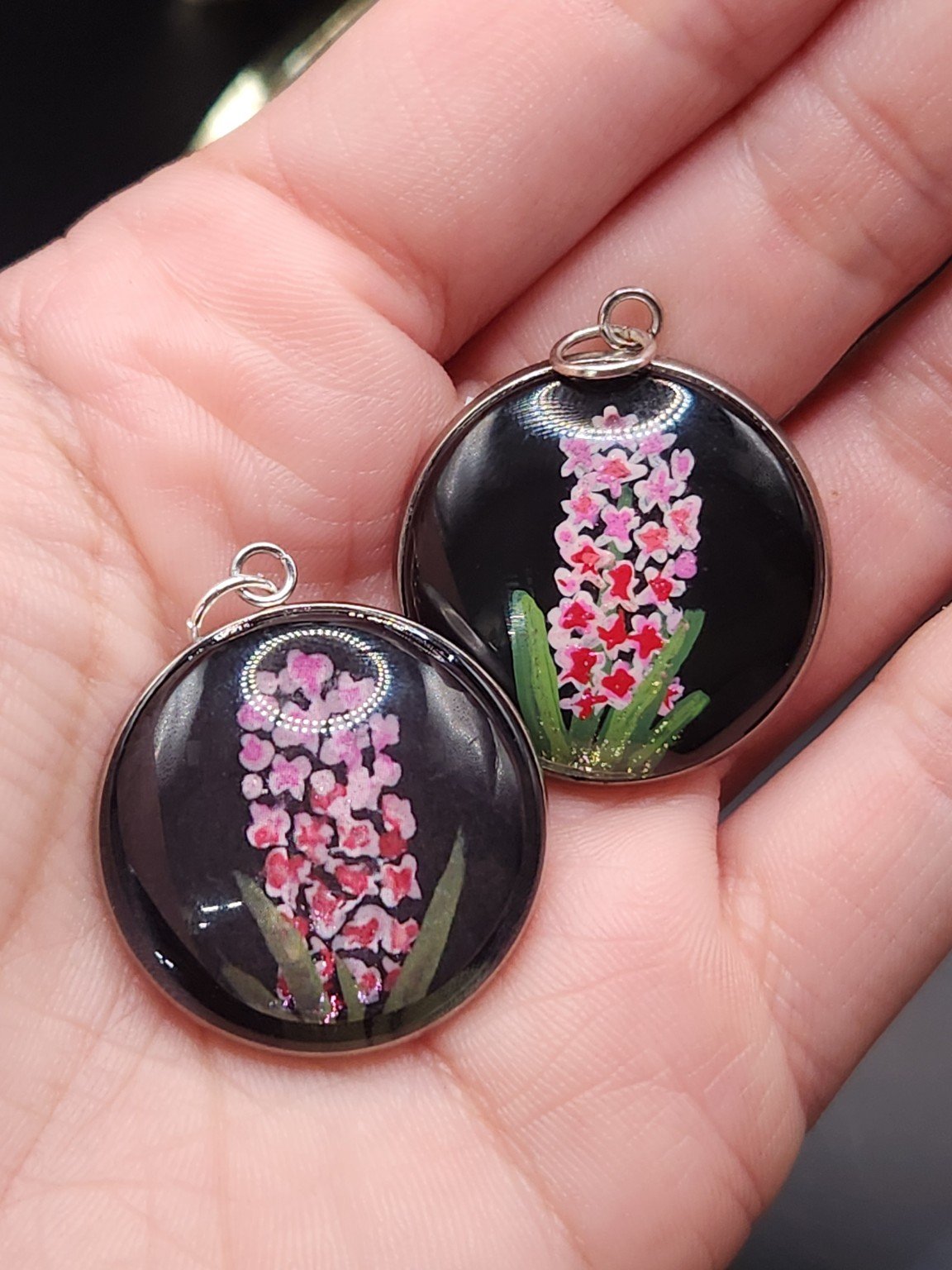 Two pink hyacinth pendants held in a hand for comparison: hand-painted original at the top right and printed reproduction at the bottom left.