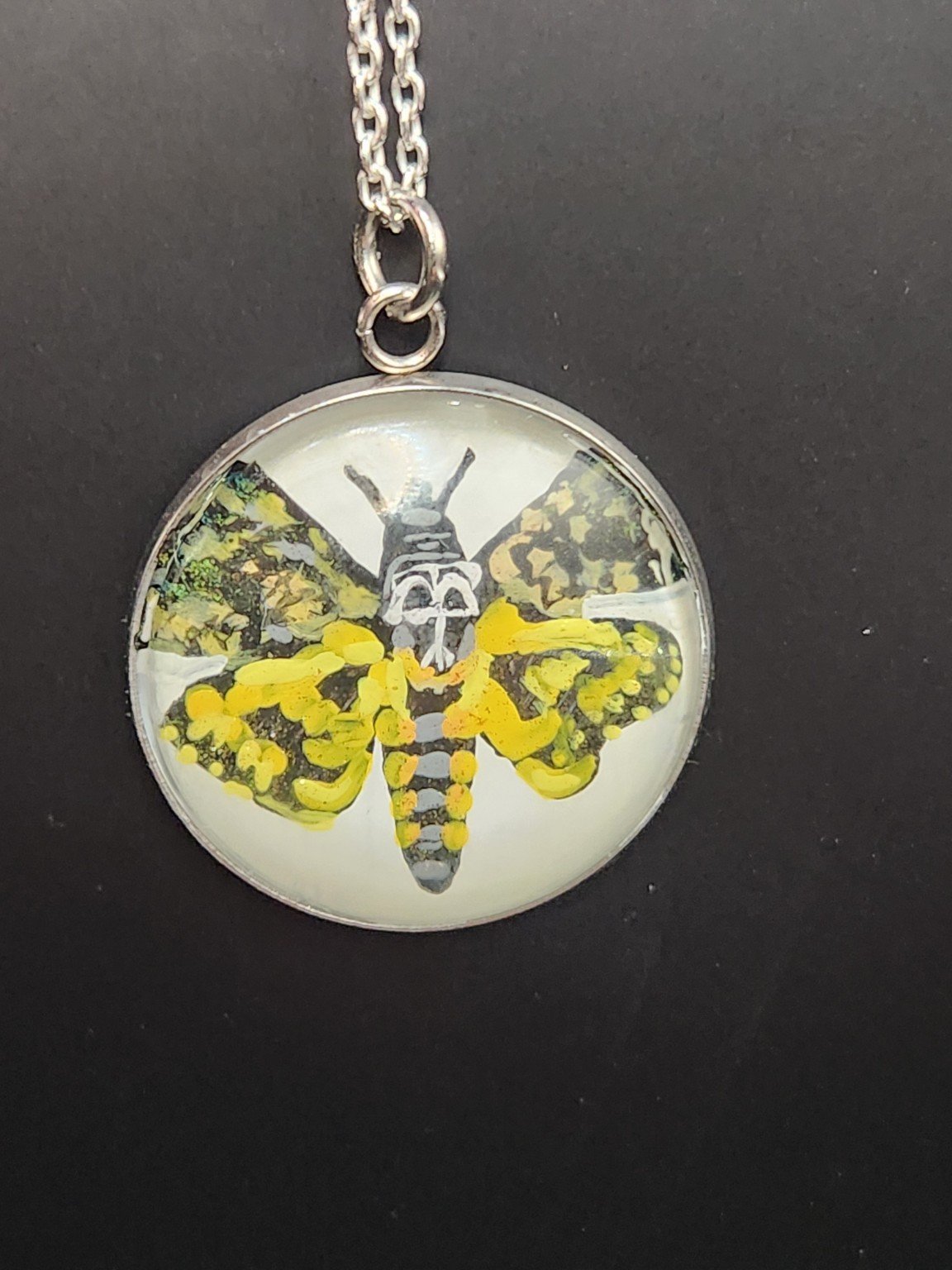 Death’s-head moth art pendant shown on a silver-tone chain against a dark background. Chain not included.