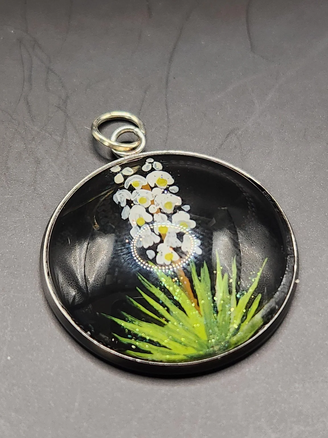 White yucca flower art pendant with yellow centers, spiky green leaves and shimmering glitter accents.