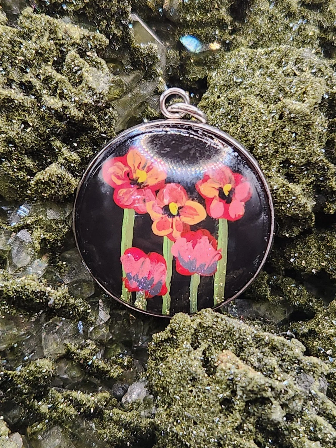 Red and pink poppy flower art pendant nestled in a sparkling green crystal display. Crystal and display props not included.